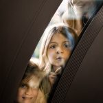 Black custom door partially visible with detailed grooves and carbon fiber detailing. Two little girls looking through the curved glass opening of the door and their mom looking down on them.
